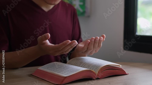 A Christian man raising open hands in praise and prayer over Holy Bible on a table indoors. Spiritual surrender, Pray to God to confess your sins and ask for blessings to overcome his problems. 
