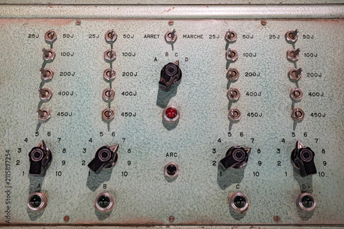 Close-up detail of a vintage analog control panel featuring toggle switches, rotary knobs, and indicator lights on a green textured metal surface.