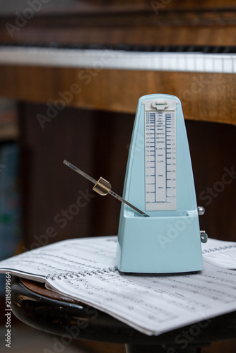 Quadro su tela Mechanical metronome on sheet music in front of an upright piano