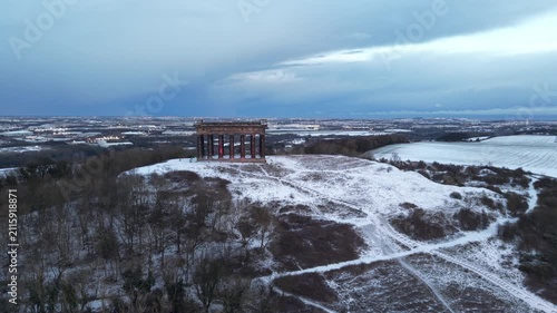 Aerial drone shot pushing slowly in toward the snow-covered Penshaw Monument in Sunderland, with the Nissan factory visible across the winter landscape in the background.