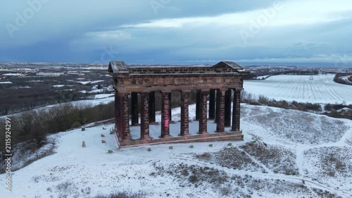 Telephoto drone orbit shot around the snow-covered Penshaw Monument in Sunderland, revealing the wider Wearside city skyline in the background.