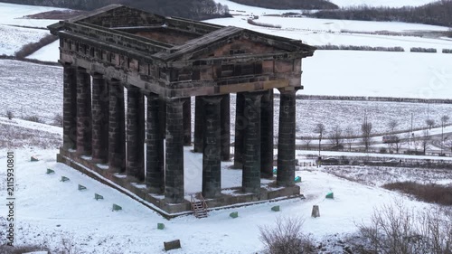 Telephoto aerial tracking shot rising over the imposing columns of Penshaw Monument in Sunderland with a snow-covered countryside background