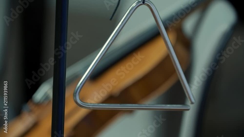 Close up of triangle musical instrument hanging with a violin in the background