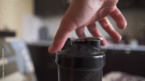 Close up of athlete hand screwing black lid on protein shaker bottle preparing fitness drink.