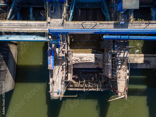 Aerial view of a dam construction site with metal scaffolding and a blue gantry crane over the water in Banyumas Regency, Central Java, Indonesia.