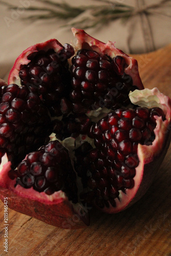 Cuadro en lienzo Ripe pomegranate fruit broken open to reveal juicy dark red seeds on a rustic wooden board, featuring moody lighting and high-contrast composition