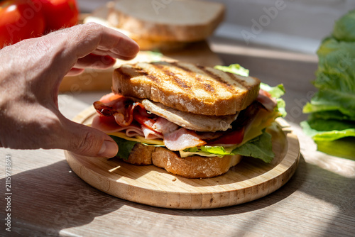 Foto Hand picking up freshly made club sandwich
