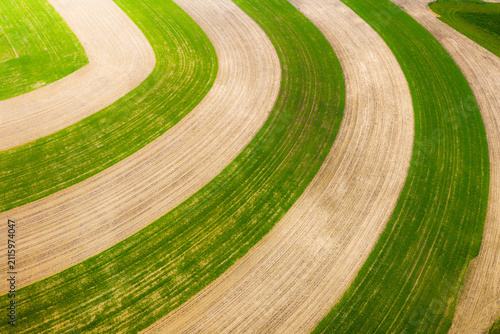 Aerial view of curved agricultural fields with alternating green crops and tilled soil patterns in Brno, South Moravian Region, Czechia.