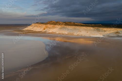 Aerial view of the dramatic white limestone cliffs of Tuzbair salt flats under a cloudy sky at sunset in Mangystau District, Mangystau Region, Kazakhstan.