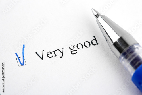 Very good checkbox marked with a blue check mark on white paper next to a ballpoint pen. Macro shot.