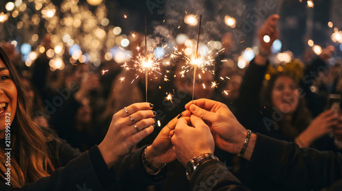 Close-up of hands holding glowing sparklers during a New Year's countdown, warm golden bokeh, festive celebration, shallow depth of field, joyful atmosphere