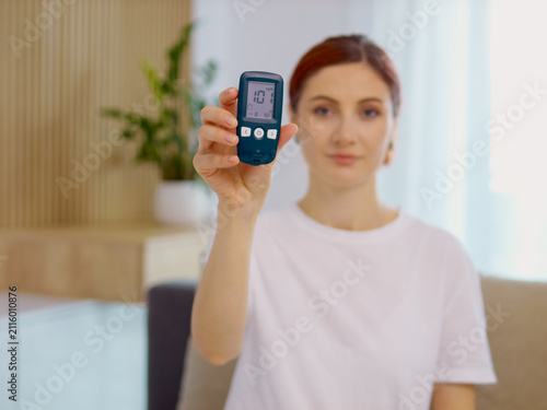 A woman shows a glucometer reading 101 mg dL in her home. She demonstrates how to use the device for monitoring blood sugar levels regularly.