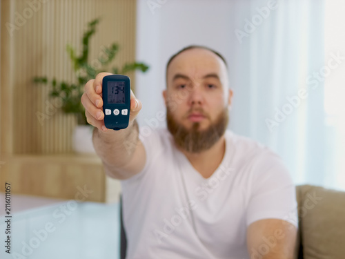 A man holds a glucometer with a reading of 134 mg dL. This reading shows a high blood sugar level. He looks concerned about his health and the implications of diabetes.