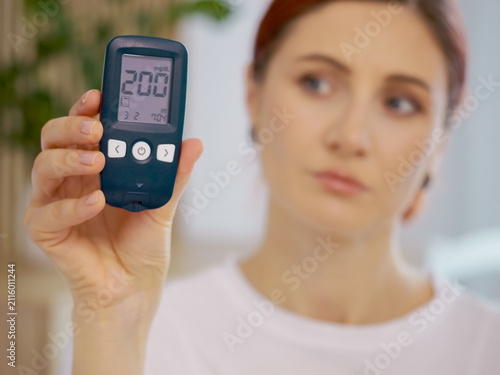 Woman holds a glucometer displaying a blood sugar level of 200 mg dL. This reading indicates a high level of glucose in her blood.