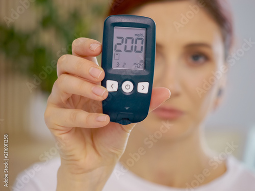 Bild auf Leinwand A woman holds a glucometer displaying a high blood sugar level of 200 mg dL