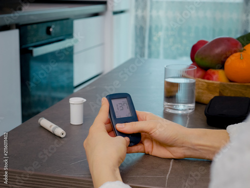 In a kitchen, a woman looks at the glucometer diary, swiping through past blood sugar results. She monitors her health by reviewing the glucose history carefully.