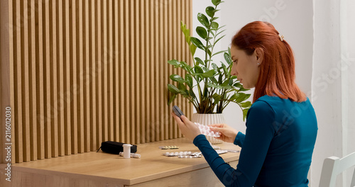 A woman takes a blood sugar test and examines the reading. She looks over at her medication on the table while making a decision about her health.