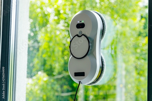 Window cleaning robot positioned on glass with green outdoor foliage in the background