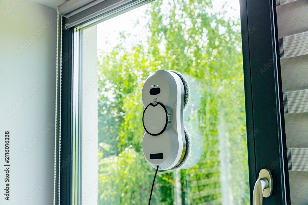 Obraz premium Window cleaning robot actively scrubbing glass surface with bright green foliage in background