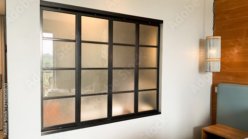 Quadro su tela Modern interior featuring a large black-framed grid window set against a clean white wall, complemented by a warm wooden accent panel and decorative wall lighting