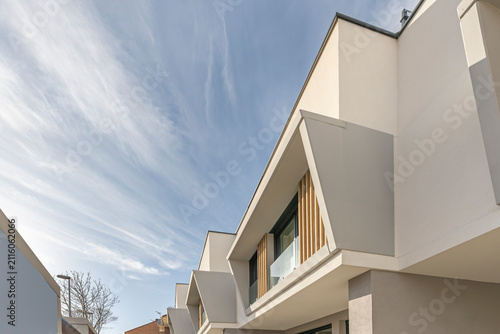 Low-angle shot of geometric white townhouse corner with slanted roofline and wooden slat window details