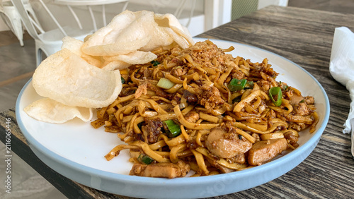 Canvastavla Close up of Delicious Indonesian kampung fried noodles served with crispy prawn crackers on a white plate at a modern café