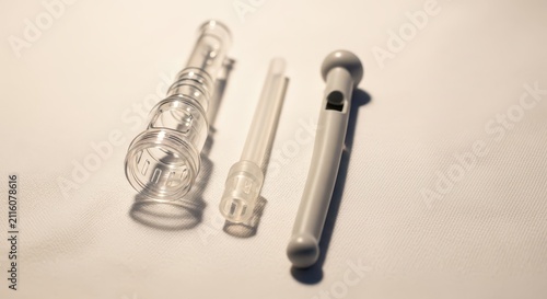 Three medical plastic components, including a clear tube and a grey plunger, isolated on a white background with soft shadows