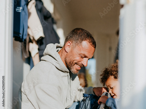 Smiling father helping his young child get ready in the hallway at home, authentic involved fatherhood and everyday family moment.