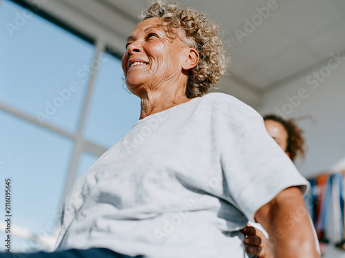 Happy senior woman with gray curly hair smiling in bright sunlight during a fitness class, joyful healthy aging and vitality concept.