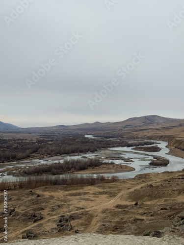 Winding river cutting through dry valley landscape with distant hills.