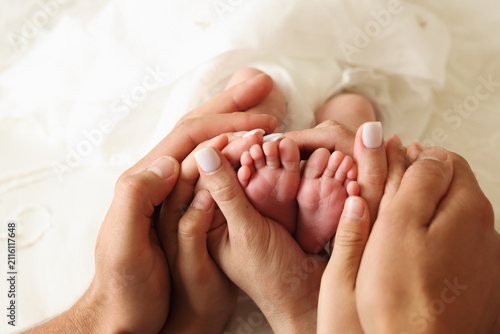 Parents gently holding their newborn baby's tiny feet in their hands. Warm family lifestyle image expressing love, care, bonding, parenthood, protection, and the beginning of a new life.
