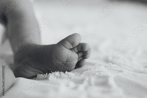 Close-up of a newborn baby's tiny foot resting on a soft blanket in natural light. Black and white image symbolizing new life, innocence, tenderness, family, and parenthood.