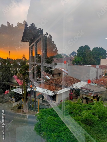 City view through glass showing a reflected orange sunset over urban roofs