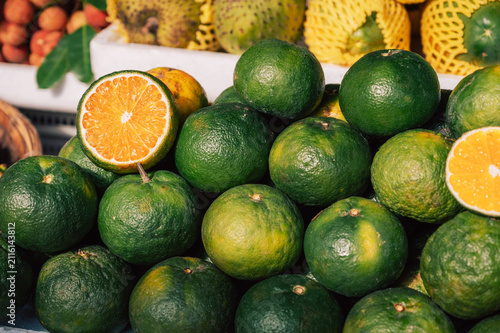 Close-up of green oranges with sliced fruit at a market, showcasing fresh citrus produce and vibrant natural colors.