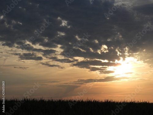 Obraz na płótnie Sunlight breaks through the dark clouds, casting golden and orange tones across the horizon