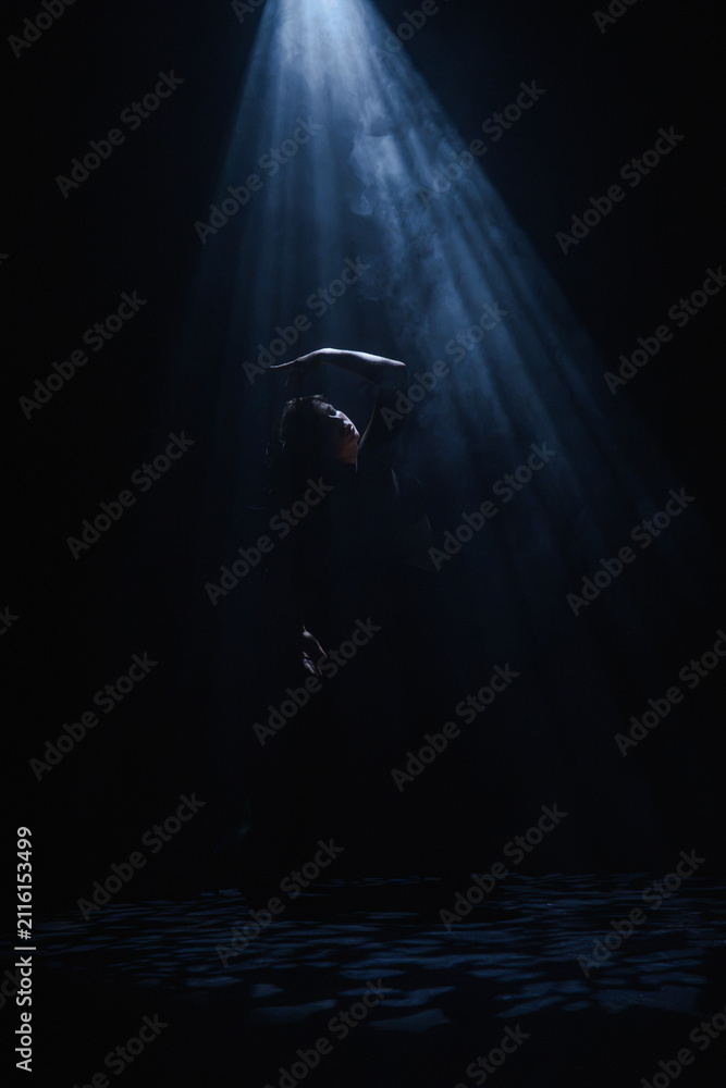 Obraz premium Mysterious silhouette of a female dancer under a blue spotlight beam. Concept of commercial template with copy space for musical show promo, theater poster and mental health therapy.