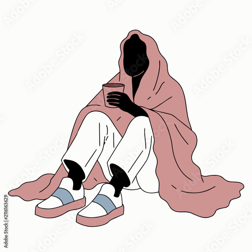 Person sitting on floor draped in blanket and holding a cup  