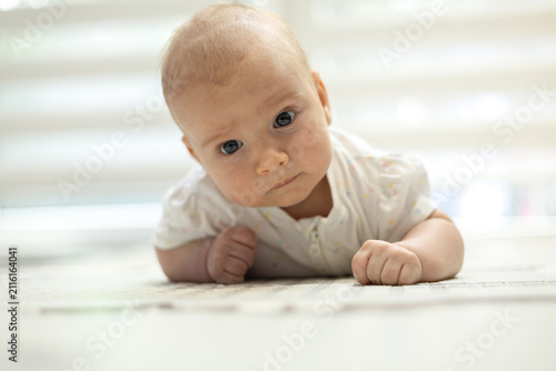 Adorable infant lying on tummy on a rug, looking curiously at the camera during tummy time at home.