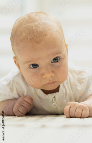 Vertical photo of adorable infant lying on tummy on a rug, looking curiously at the camera during tummy time at home.