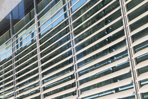 Curved exterior glass facade of a modern corporate office building featuring horizontal metal sun louvers and steel support columns reflecting sunlight.