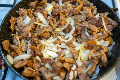 Cuadro en lienzo A top-down view shows chopped chicken gizzards and sliced white onions being fried together in a dark non-stick pan set on a gas stove