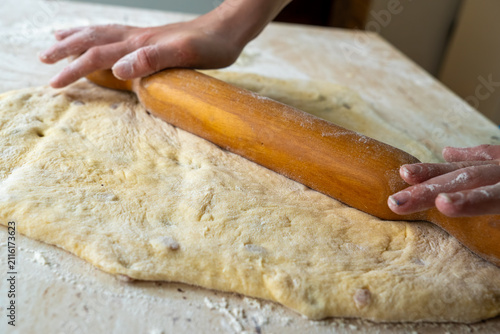 Cuadro en lienzo Female hands flatten fresh yeast dough on a flour-dusted table using a classic wooden rolling pin to prepare home-baked pastry