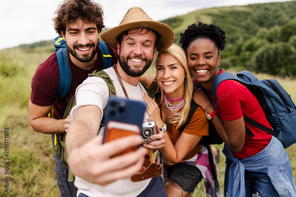 Obraz premium A group of four friends joyfully poses for a selfie in a scenic outdoor setting, surrounded by lush greenery, capturing a moment of fun and camaraderie.