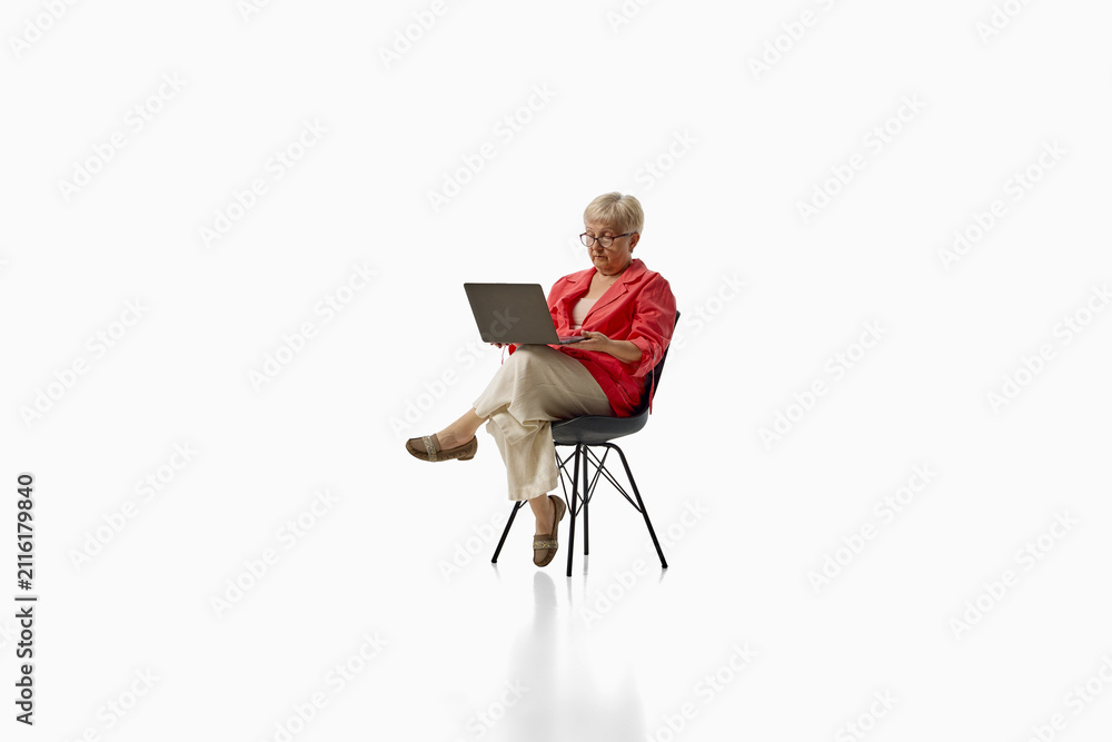 Fototapeta premium Senior woman working on laptop while seated isolated on white background. Concept of digital inclusion, remote work, lifelong learning.