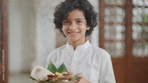 Happy Indian boy in white kurta holding a traditional puja thali