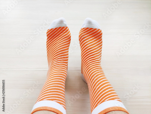 Feet wearing soft knitted patterned socks on a light wooden floor. Cozy domestic shot from a side view, concept of comfort, warmth, relaxation, leisure, and casual home fashion
