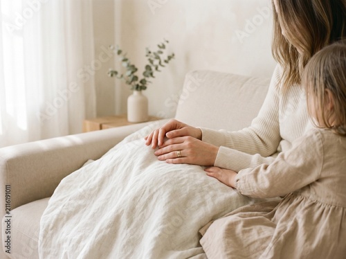 Mother and daughter sitting on a sofa. Loving parent holding child hand in cozy home.
