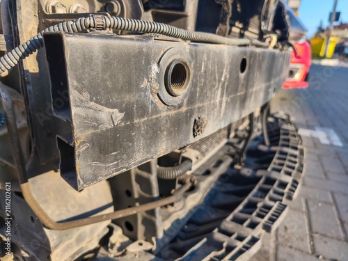 Closeup of exposed front vehicle frame and radiator support during automotive collision repair with dismantled body panels in outdoor workshop