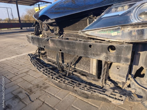 Front section of damaged passenger car with removed bumper exposing structural frame during professional automotive collision repair process outdoors