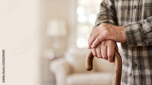 Closeup of an elderly mans hands resting on a wooden walking cane